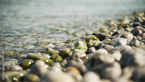 Waves breaching the shore on a stone beach during a sunny day. Extreme slow motion. photo