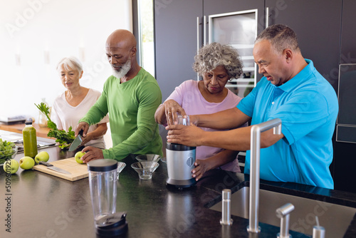 Foto Multiracial seniors preparing smoothie with granny smith apples and leaf vegetab