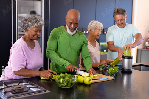 Multiracial seniors friends chopping fruits, vegetables and blending smoothie on kitchen counter