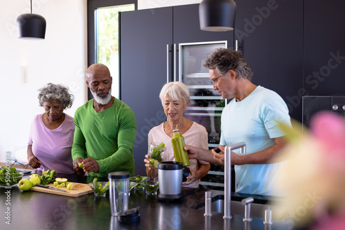 Multiracial senior friends making fruits and leaf vegetables smoothie in kitchen at retirement home