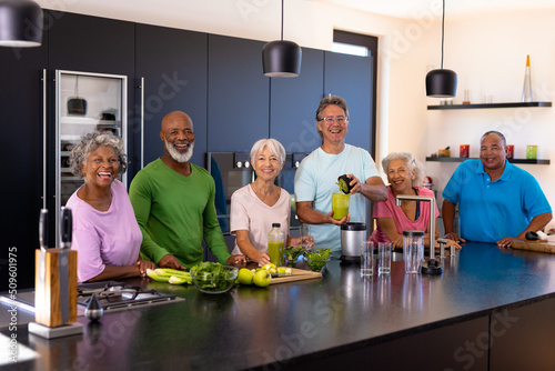 Portrait of cheerful multiracial senior friends preparing smoothie in kitchen at retirement home
