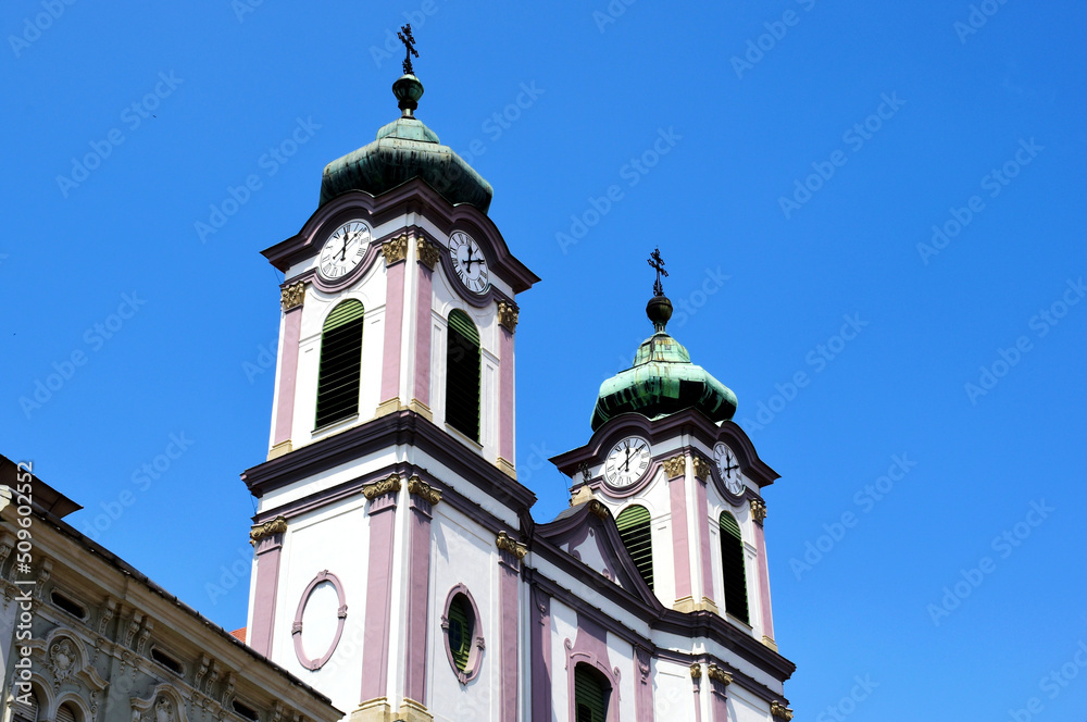 Baroque style double church towers with clock and bell tower in diminishing perspective. Szekesfehervar, Hungary. aged and weathered green copper metal roofs. blue sky.  travel and tourism concept