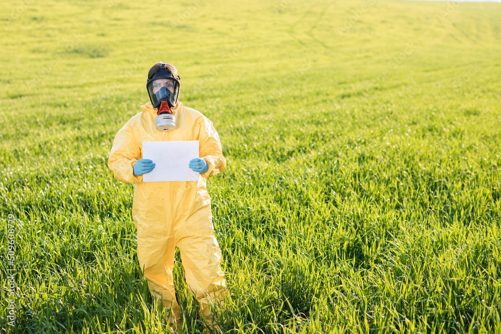 Person in overalls and gas mask holds holds a sheet of paper with the exclamation Save the Planet while standing on green field on sunset. Person in overalls and gas mask holds holds a sheet of paper with the exclamation Save the Planet while standing on green field on sunset.