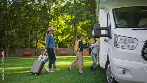 Side view of young family with suitcases going to caravan outdoors at park.