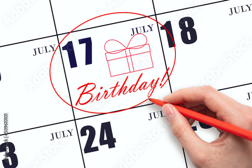 The hand circles the date on the calendar 17July, draws a gift box and writes the text Birthday. Holiday. photo