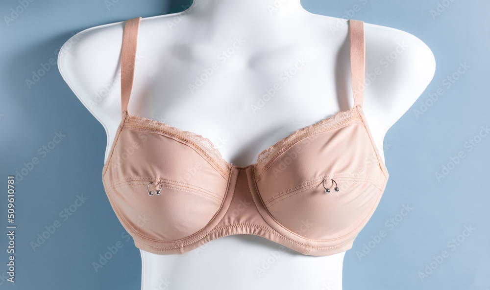 Beige bra on white mannequin with metal rings. Nipple piercing concept.  Stock Photo