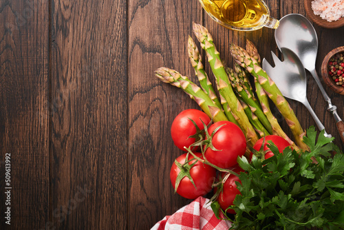 Parsley, parsley, tomato, garlic, olive oil, pepper, salt and salad fork and spoon on wooden cooking background. Food cooking background. Ingredients for cooking food background. Mock up. Top view.