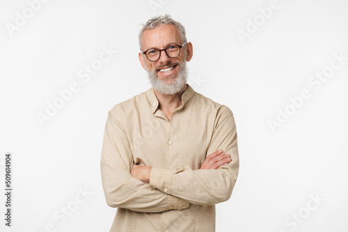 Smart caucasian mature middle-aged freelancer man in beige shirt wearing glasses looking at camera with arms crossed isolated in white background