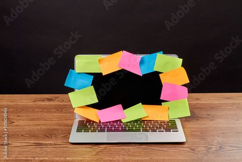 Open laptop with many colored sticker notes for copy space. Notebook on a brown wooden desk.