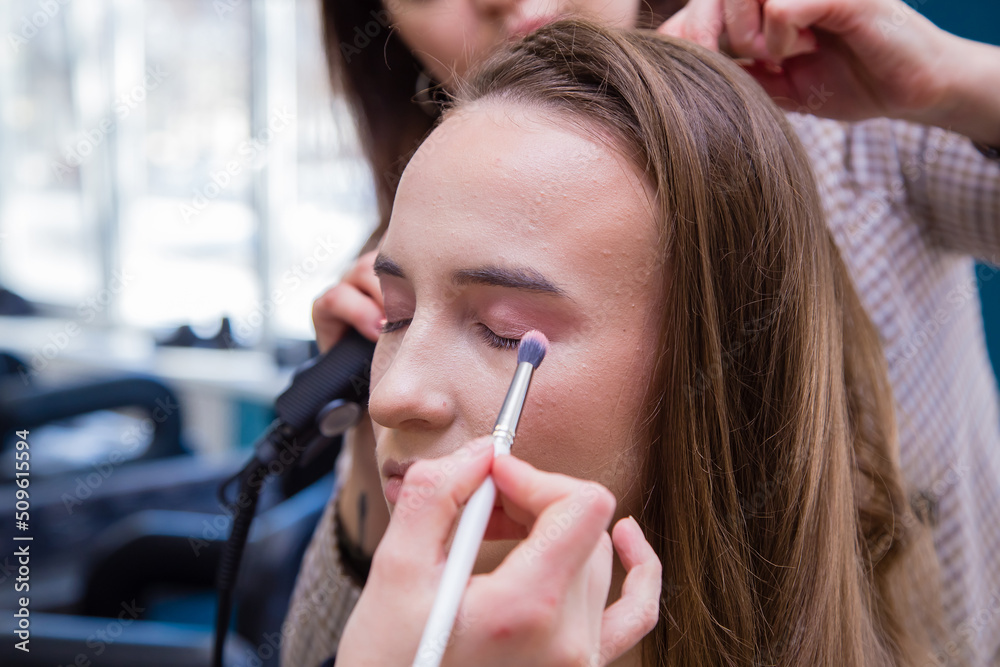 Close-up of a hand with a brush paints the eyelid of a girl in a salon. Female master makes makeup to a young woman. Business concept - beauty salon, facial skin care, cosmetology. Close-up of a hand with a brush paints the eyelid of a girl in a salon. Female master makes makeup to a young woman. Business concept - beauty salon, facial skin care, cosmetology.