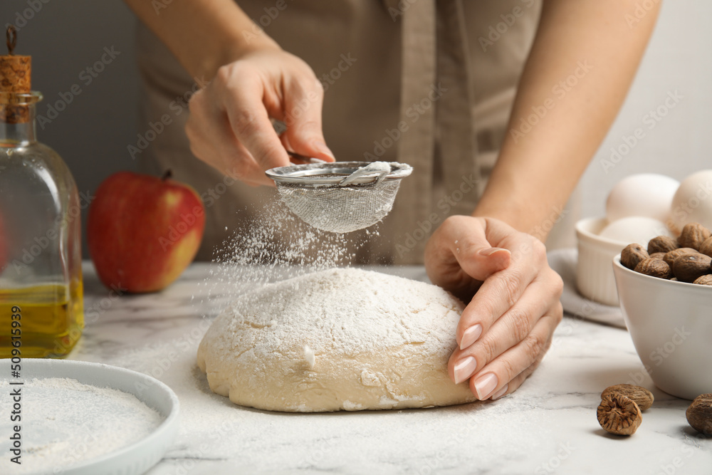 Fototapeta premium Woman sprinkling flour onto dough at white marble table, closeup