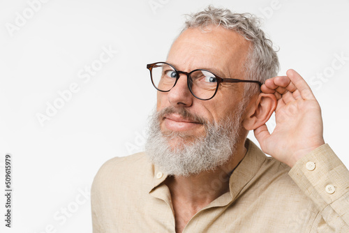 Closeup cropped curious mature middle-aged man pricking up ears, listening to gossips rumors, hand to ear isolated in white background. Secret, sale, discount