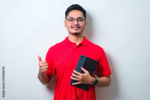 Potrait of cheerful young guy wearing casual shirt and glasses using tablet and showing thumbs up