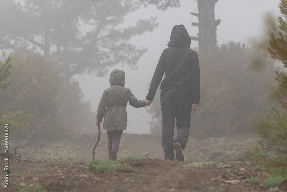 Selective focus shot of mother and daughter on dirt forest road in nature.