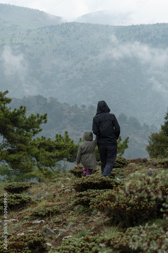Selective focus shot of mother and daughter standing on mountainside in foggy weather while looking at landscape. Selective focus shot of mother and daughter standing on mountainside in foggy weather while looking at landscape.