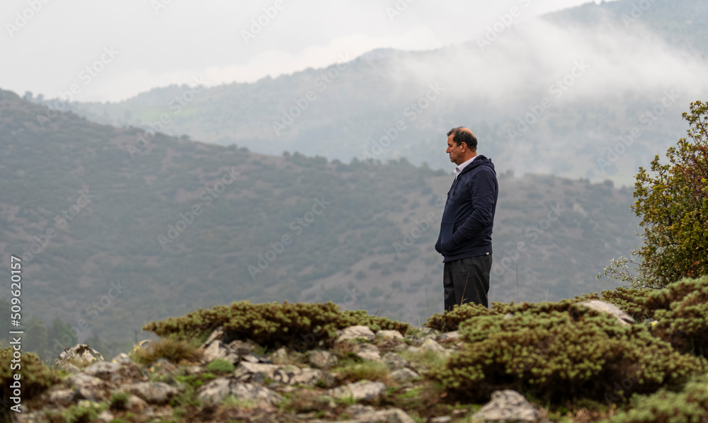 Selective focus shot of depressed old man standing on scree and looking at the foggy landscape.