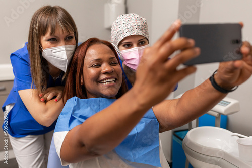A black woman patient, takes a happy selfie photo with the smartphone side by side the dentist and dental hygienist at the dental clinic photo