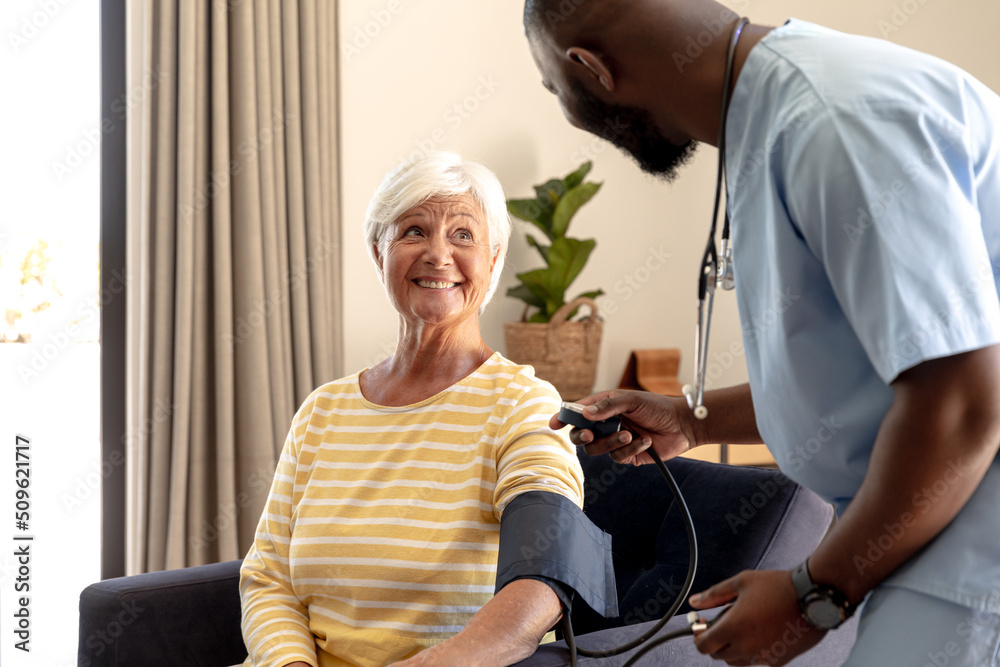 Obraz premium African american male health worker checking blood pressure of caucasian senior woman at home