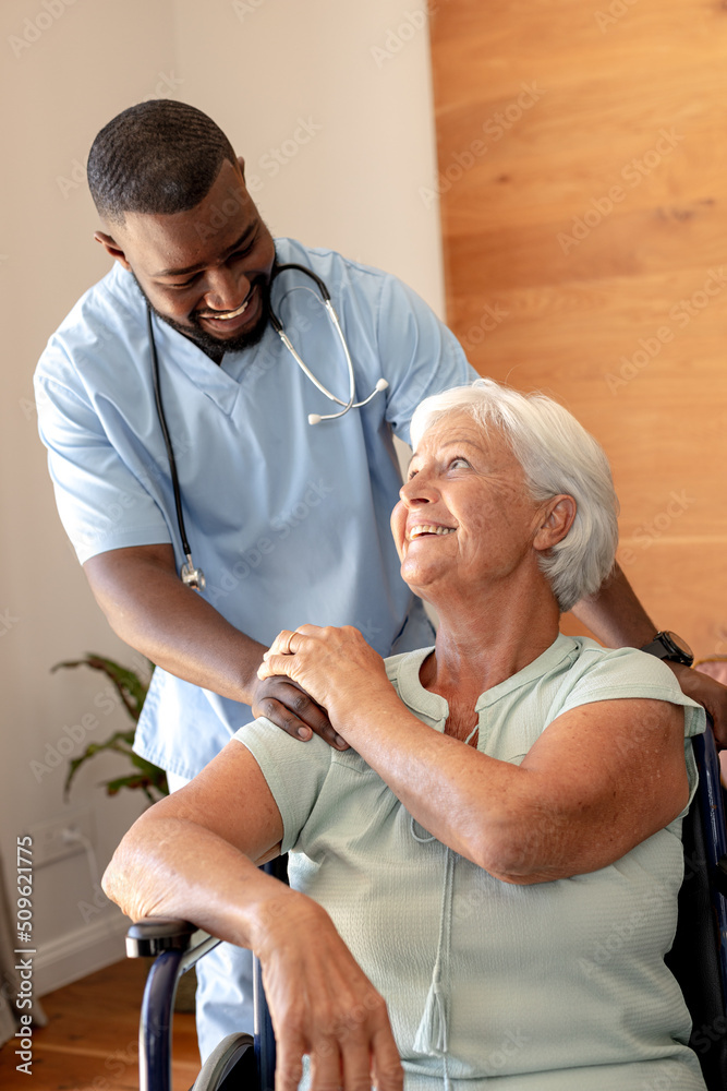 Obraz premium African american male health worker supporting caucasian senior woman sitting on the wheelchair