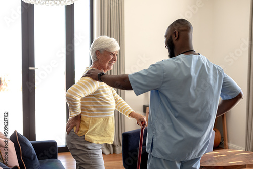 African american male health worker helping caucasian senior woman to walk using a walking stick