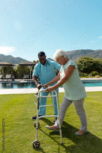African american male health worker helping caucasian senior woman to walk with a walking frame