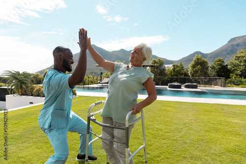 African american male health worker and caucasian senior woman high fiving each other in the garden