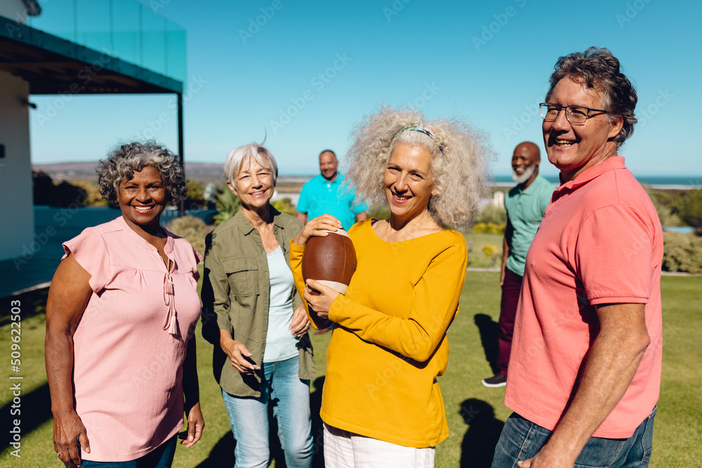 Portrait of happy multiracial senior friends playing rugby in yard against clear sky at nursing home Portrait of happy multiracial senior friends playing rugby in yard against clear sky at nursing home