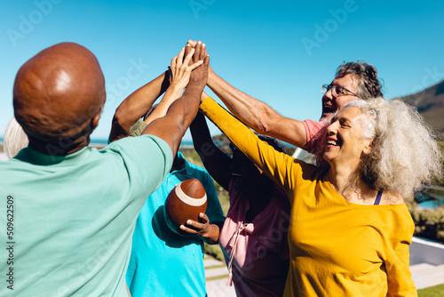 Multiracial seniors giving high-five while playing rugby against clear sky in yard at nursing home