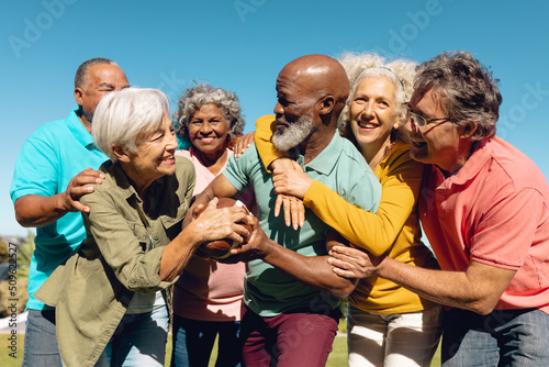 Multiracial senior friends striving to get rugby ball against clear sky in yard at nursing home