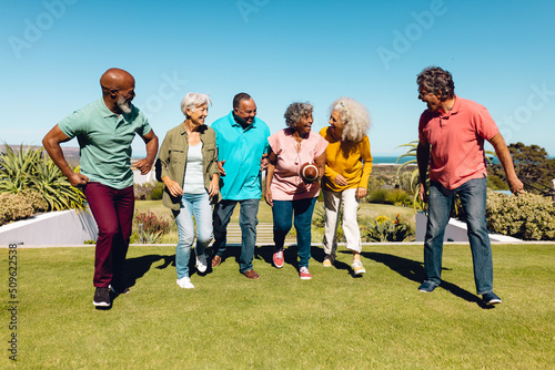 Cheerful multiracial seniors playing rugby in yard against clear blue sky at retirement home