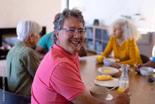 Portrait of happy caucasian senior man having breakfast with multiracial friends at dining table