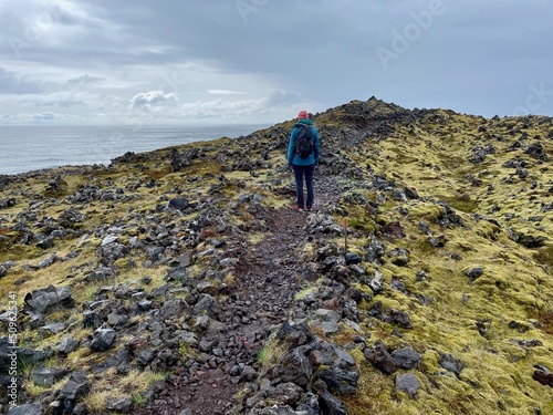 Woman hiking on coastal path from Djupalonssandur to black beach of Dritvik in Snaefellsnes Peninsula, Iceland. photo