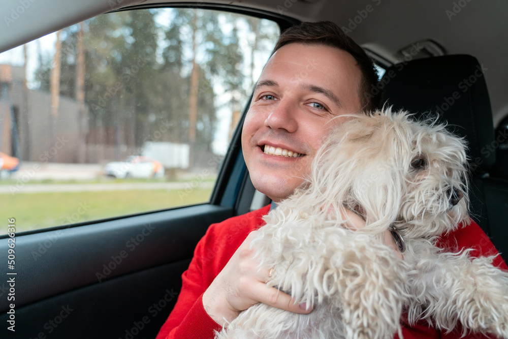 Happy man hugs his white lapdog and smiles at camera. Owner of a fluffy Chinese crested dog travels by car. Travel with pet concept. Happy man hugs his white lapdog and smiles at camera. Owner of a fluffy Chinese crested dog travels by car. Travel with pet concept.