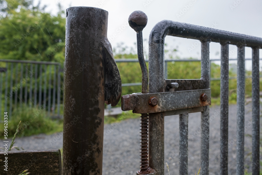 Metal gate with a latch, limiting the passage to the fenced area, outdoors. 