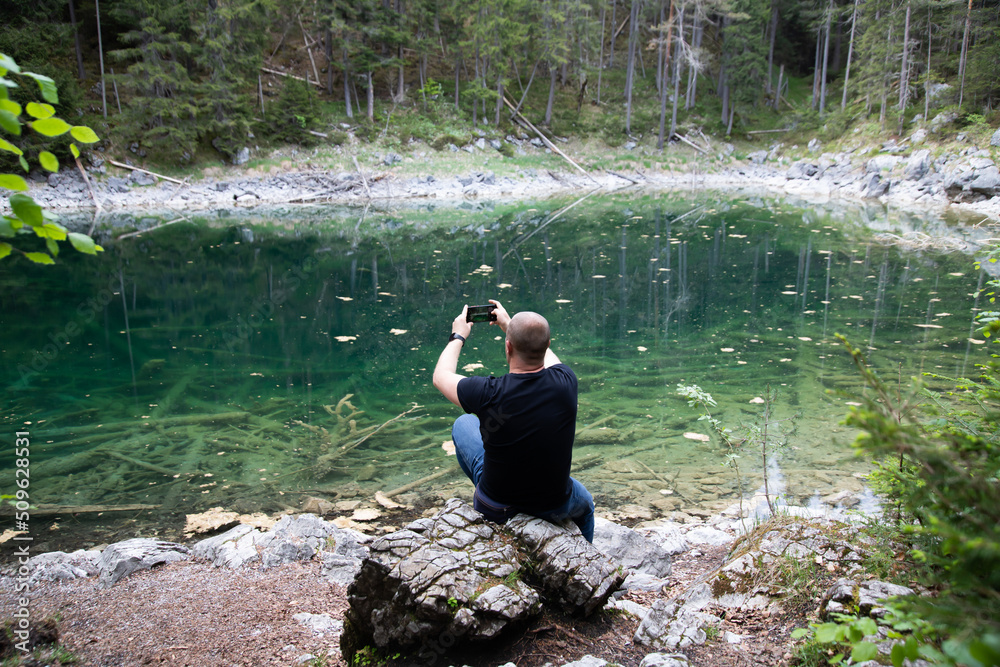 Young man sitting on a stone near the Eibsee Lake, Germany. Travel, lifestyle concept.