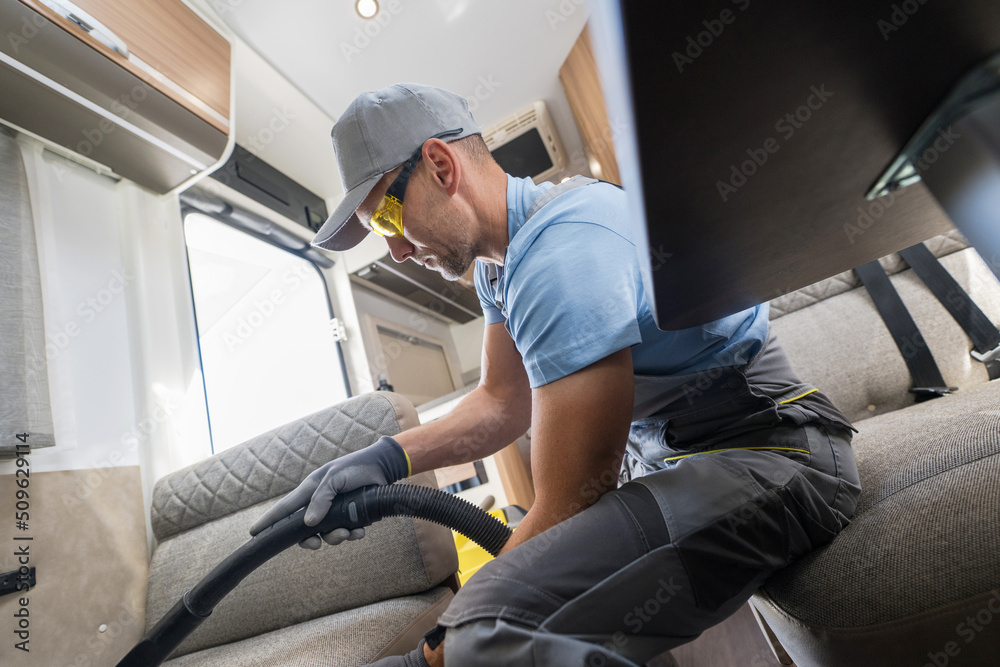 Man Vacuuming a Sofabed in a Recreational Camper Van Man Vacuuming a Sofabed in a Recreational Camper Van