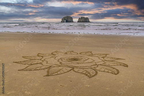 Intricate mandala star sand design on the ocean beach with Twin Rocks in the ocean and beautiful sky. photo