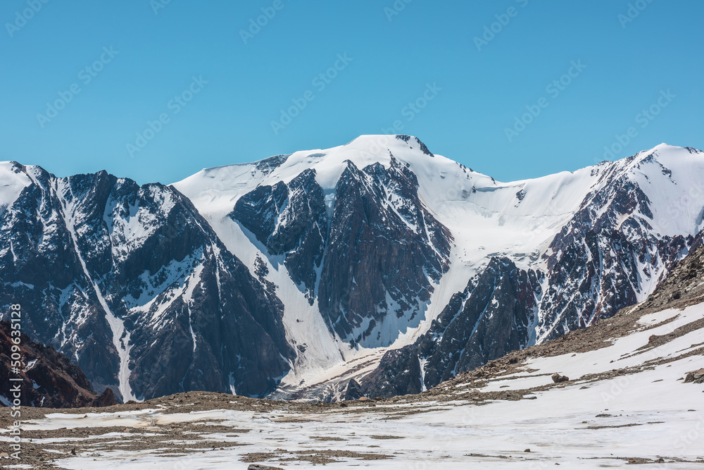Scenic landscape with snowy mountain top. Wonderful view from stonу snowу mountain to mountain range under blue sky in sunny day. Awesome scenery with snow mountains in sunlight at very high altitude.