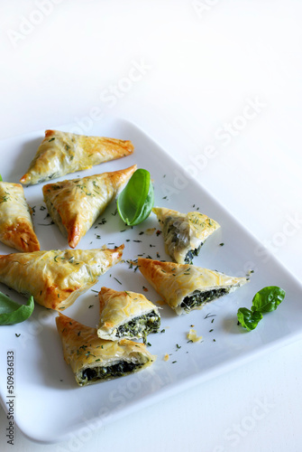 Cucina tradizionale greca. Spanakopita, triangolo di pasta fillo con spinaci e feta su sfondo bianco. Direttamente sopra.