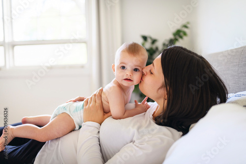 Mother and baby on white bed at home gaving a kiss