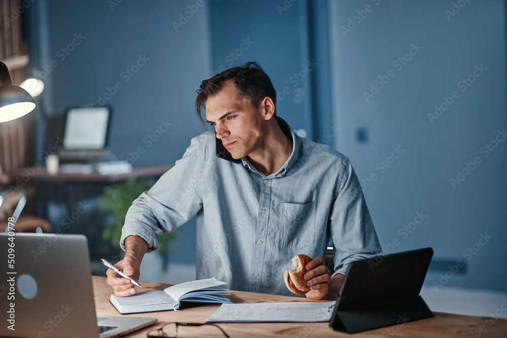 young businessman snacking on a hamburger while working on a new project.