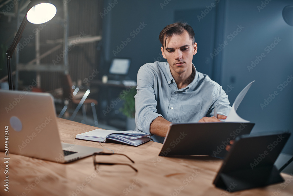 young businessman taking notes in a notebook in a night office. young businessman taking notes in a notebook in a night office.