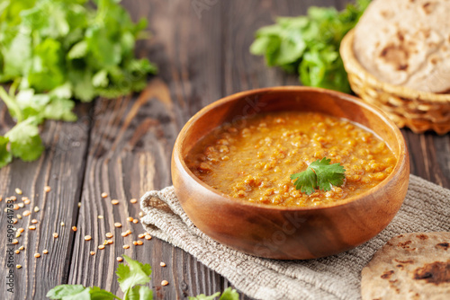 Indian dal food (Masoor Dal or Dal Tadka Curry) and homemade Flatbread Chapati. Traditional Indian soup lentils. Indian Dhal spicy curry in bowl, spices, herbs, rustic black wooden background. photo