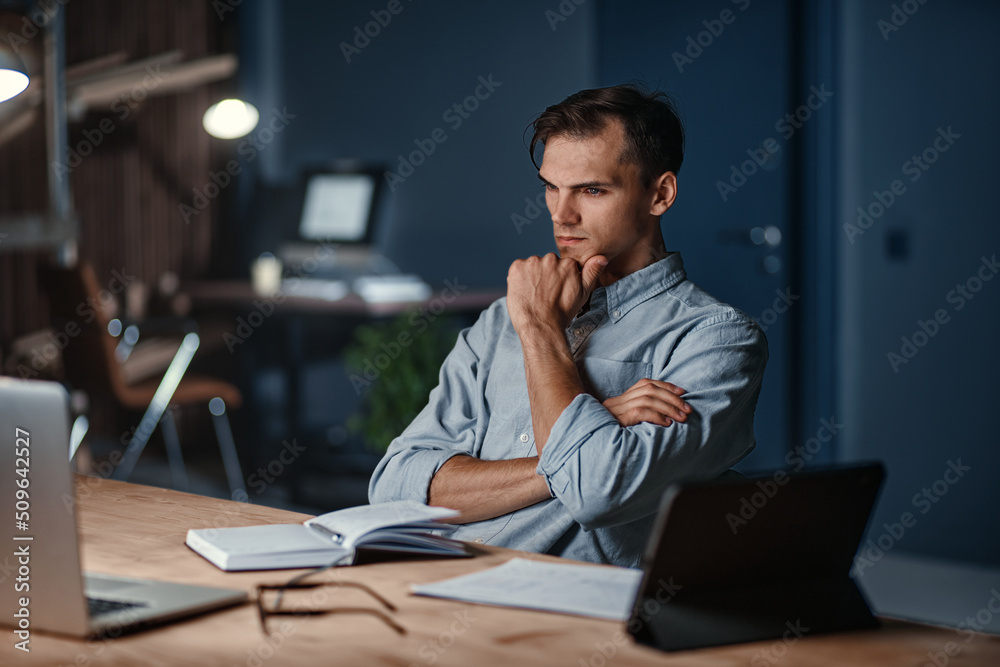 thoughtful tired businessman sitting at his desk at night in the office. thoughtful tired businessman sitting at his desk at night in the office.