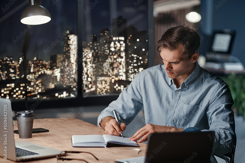 tired businessman taking notes in his diary late at night.