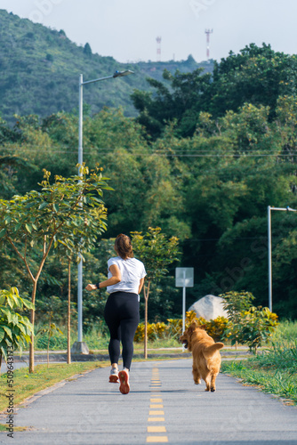 beautiful woman running doing sports and cardio in the central park accompanied by her pet a golden retriever