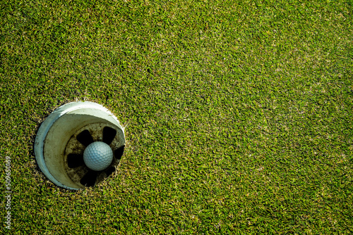 Golf ball in hole on a green lawn in a beautiful golf course with morning sunshine.