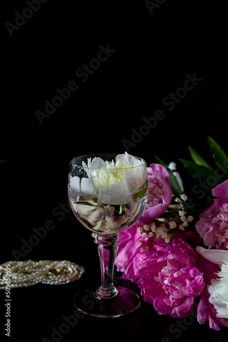 wine and flowers. still life with flowers. Bouquet of white and pink peony on a black background. Pearl necklace. Flower in a glass of water