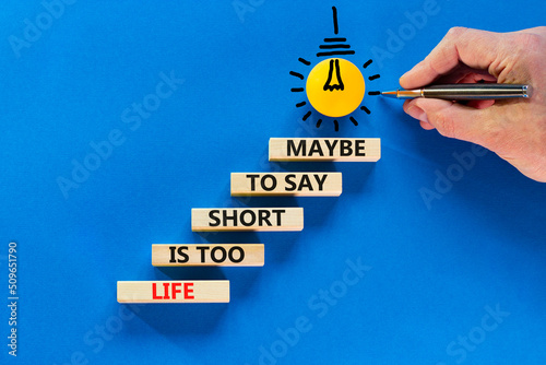 Life is short for maybe symbol. Concept words Life is too short to say maybe on wooden blocks on a beautiful blue table blue background. Businessman hand. Business motivational life or maybe concept.