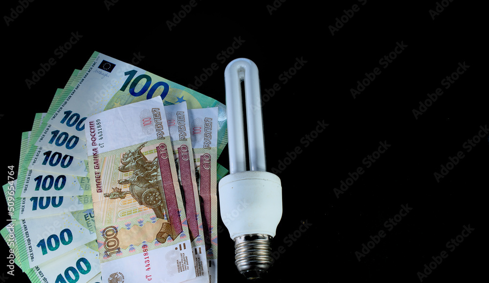 Close-up of euro, Russian ruble and energy saving light bulb on black background.
High quality photo. Income and business concept.